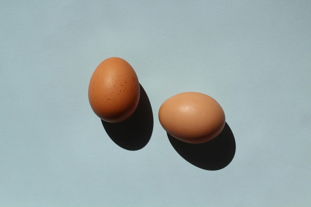 A minimalist composition of two brown eggs casting shadows on a pastel blue background.